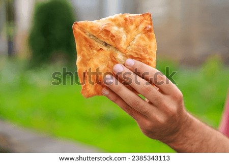 Guy's hand holds a puff pastry with cheese, snack and fast food concept. Selective focus on hands with blurred background and copy space for text. Royalty-Free Stock Photo #2385343113