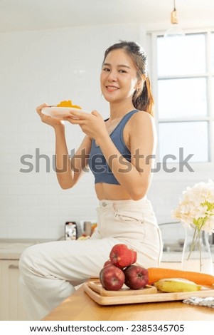 A healthy Asian woman in exercise clothes Is happily cooking a healthy meal in her home kitchen in the morning. Healthy care concept, Healthy fruits every day. Royalty-Free Stock Photo #2385345705