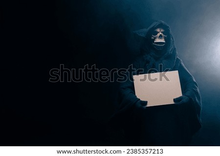 Skeleton, skull, silhouette of a man in a black robe, depicting death holding a blank poster. The scary grim reaper. Death Grim Reaper Costume for Halloween. blue toning photo