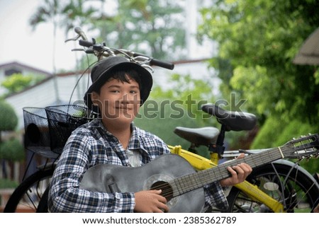 Asian boy is playing acoustic guitar in the schoolpark happily, soft and selective focus, concept for happiness of children with popular instruments around the world.