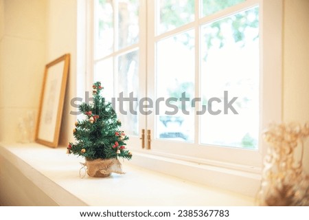 Decorate christmas event on counter by the bright window with small chrismas tree and wooden picture frame on the back