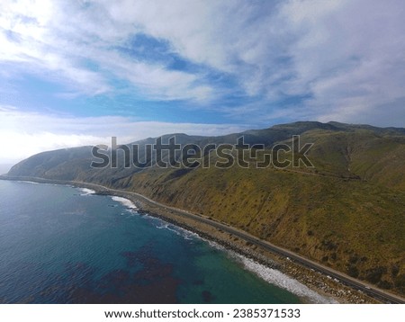 aerial shot of a gorgeous summer landscape along the coast of California with vast blue ocean water, waves and rocks along the beach with blue sky and clouds at sunset