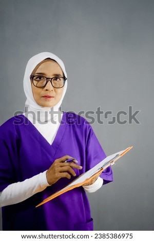 Nurse wearing hijab, Asian hijab Nurse wearing purple medical uniform holding folder or paper board writing, checking.