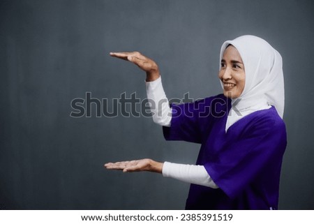 Asian hijab nurse wearing purple medical uniform pointing or showing on her right side. Design for Healthcare and medical brochure or banner.