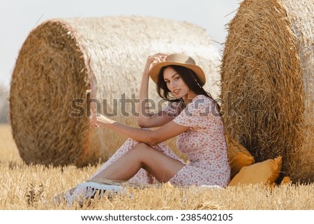 A girl in a dress with a hat near a haystack.