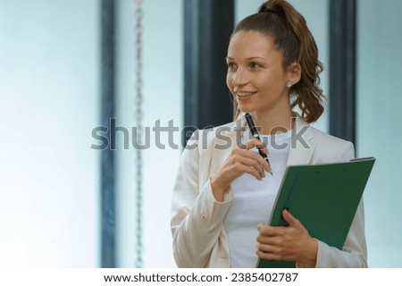Businesswoman holding folder for paper write marker thinking dreaming standing near office table.