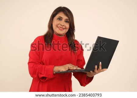 smiling Indian businesswoman working on laptop in hand wearing red corporate dress while isolated on studio background. Asian corporate female.