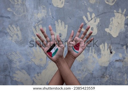 Man shows crossed arms painted with Palestinian flag and watermelon slices with hand prints on the wall in the background. Stop war and humanity concept Royalty-Free Stock Photo #2385423559