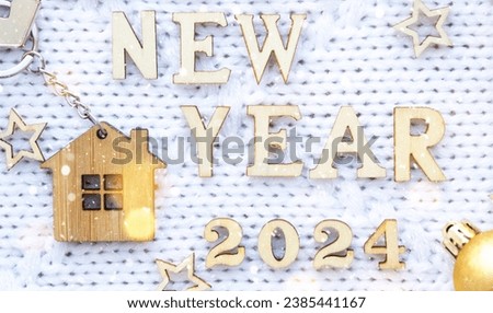 House key with keychain cottage on cozy festive knitted background with stars, bokeh. Happy New Year 2024 wooden letters, greeting card. Purchase, construction, relocation, mortgage, insurance