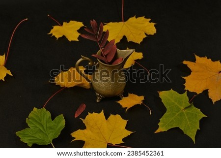 Autumn decoration with a maple leaf's and bronze saucer cup. Black background. Not edited picture.  Brass cup with a maple leaves in a background. 
