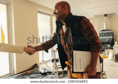 Happy mature contractor shakes hands with a homeowner after signing the paperwork, finalizing a home renovation deal. A successful collaboration for an indoor remodel and improvement project. Royalty-Free Stock Photo #2385456893