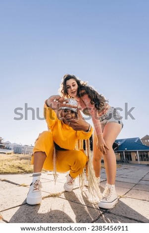 Girl making a frame gesture with her hands while looking at the camera. Two female best friends friends having fun together outdoors in the city. Happy female youngsters feeling vibrant. Royalty-Free Stock Photo #2385456911
