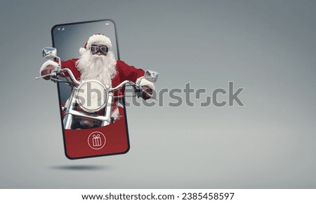 Unconventional bad Santa Claus riding a motorcycle and coming out of a smartphone screen, Christmas and technology concept Royalty-Free Stock Photo #2385458597