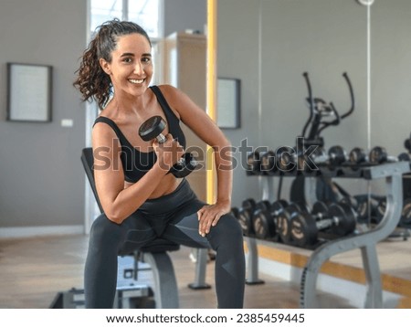 Beautiful athletic muscular woman pumps up the muscles by one arm lifts dumbbell exercise in fitness. Young healthy woman in sportswear doing exercise in fitness.   Royalty-Free Stock Photo #2385459445
