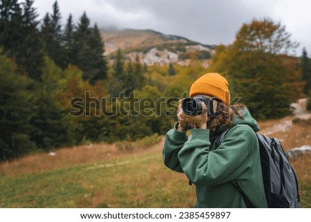 Woman traveler photographer taking photo using camera during autumn trip to mountains and forest