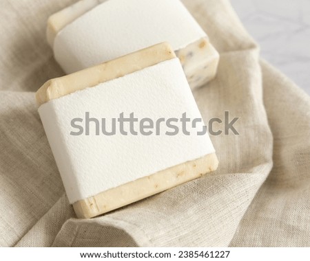 Beige handmade soap bars with blank label on linen towel close up, mockup, copy space. Natural herbal products for face and body care Royalty-Free Stock Photo #2385461227