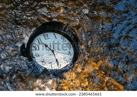 Concept image losing track of time, relativity science image, flowing time, large clock in a flowing stream with half of the clock face submerged with ripples, pebbles and distorted numbers Royalty-Free Stock Photo #2385465661