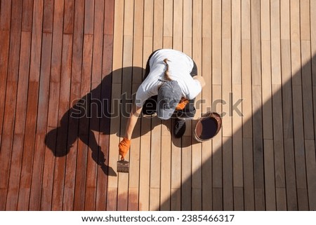 Coating with protective outdoor UV wood oil on the wooden surface of the lining boards, worker with paintbrush overhead view Royalty-Free Stock Photo #2385466317