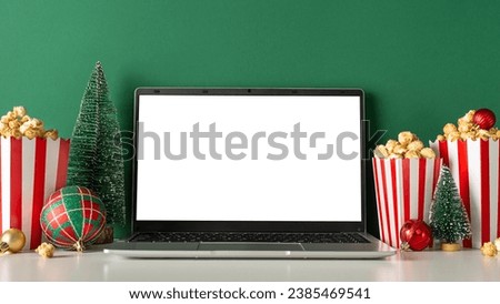 Spend your winter holidays indoors, streaming films. On a green wall backdrop, from side view, a laptop, popcorn, baubles, and a small fir tree set the mood