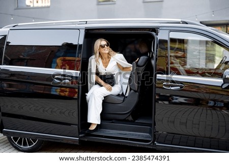 Elegant business lady in white looks out of a minivan taxi. Concept of business trips and transportation Royalty-Free Stock Photo #2385474391