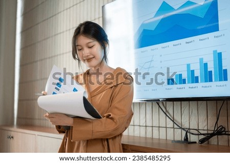 A beautiful young Asian businesswoman or female financial analyst is reading information in her paperwork while presenting her financial analysis information in the meeting. Royalty-Free Stock Photo #2385485295