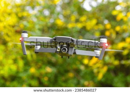 Drone with digital camera and fast rotating propellers flying taking video and pictures. Greenery backgroud
