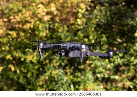 Drone with digital camera and fast rotating propellers flying taking video and pictures. Greenery backgroud