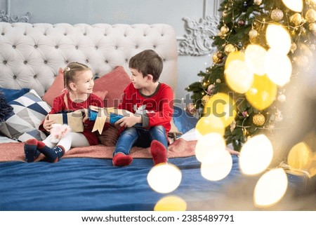 Christmas morning. The little girl opened the box with a Christmas present. She is sitting in his pajamas on the bed and smiling happily. Brick wall is decorated with Christmas lights. Happy Christmas