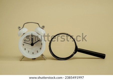 A white alarm clock sitting next to magnifying glass isolated on yellow background