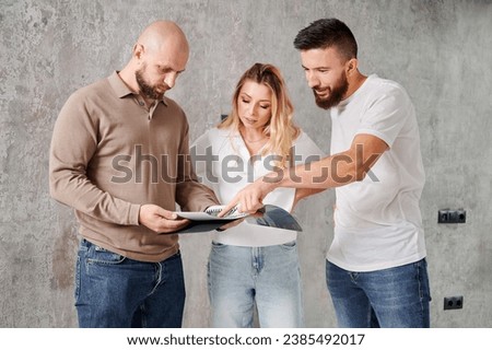 Man and woman looking at catalogue while choosing interior design for new apartment with professional designer. Couple planning home renovation and redesigning with specialist. Royalty-Free Stock Photo #2385492017