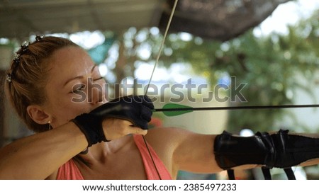 Sport woman in shooting range with bow. Outdoor archery training. Practice and training of archery in shooting range. Athlete keep wooden bow. Sportsman in shooting gallery aim an arrow to hit target Royalty-Free Stock Photo #2385497233