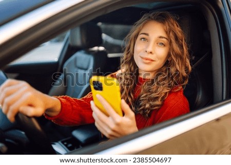 A woman driver uses a smartphone in the car. Happy woman in the driver's seat using navigation to move around. Concept of travel, technology, internet. Leisure activities.
