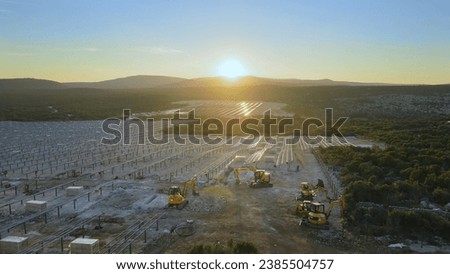 Aerial view over machinery at a solar farm construction site, during sunset