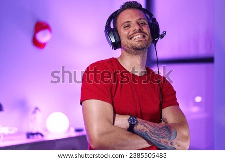 Young hispanic man streamer smiling confident standing with arms crossed gesture at gaming room Royalty-Free Stock Photo #2385505483