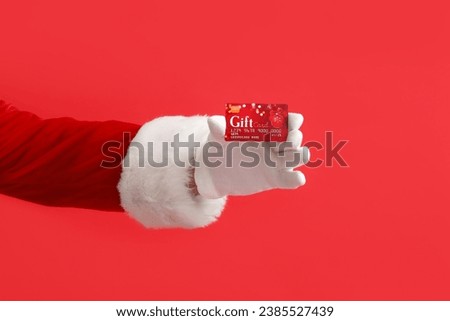 Santa Claus with gift card on red background Royalty-Free Stock Photo #2385527439