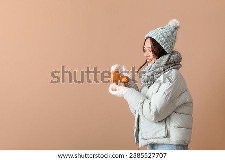 Beautiful young Asian woman in warm scarf with decorative mushrooms on brown background