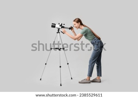 Young astronomer looking at stars through telescope on grey background Royalty-Free Stock Photo #2385529611