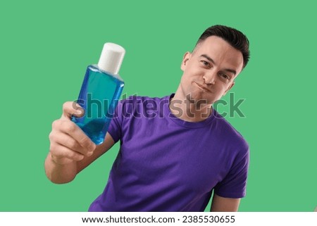 Handsome man with mouth rinse on green background, closeup Royalty-Free Stock Photo #2385530655