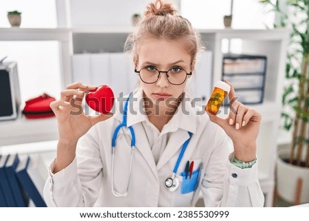Young caucasian doctor woman holding pills and heart skeptic and nervous, frowning upset because of problem. negative person. 