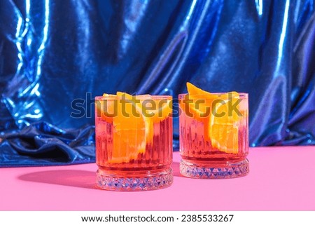 Glasses of cold Negroni cocktail and shiny fabric on pink background