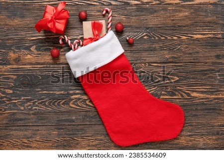 Christmas sock with balls, gift boxes and candy canes on wooden background