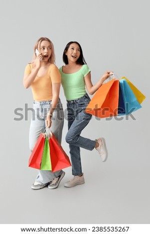 Beautiful young women holding shopping bags and talking by mobile phone on white background