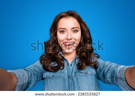 Self-portrait of nice cute stylish trendy flirty cheerful lovely attractive adorable brunette girl with wavy hair in casual denim shirt, showing tongue out, isolated over grey background