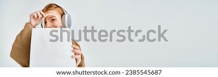 jolly little girl with headset and present bag in front of her face, fashion concept, banner Royalty-Free Stock Photo #2385545687