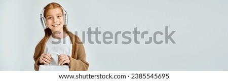 happy little girl with headset holding present bag and smiling at camera, fashion concept, banner Royalty-Free Stock Photo #2385545695