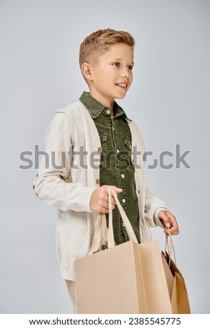 vertical shot in profile of preteen cute boy in casual attire holding present bags, fashion concept Royalty-Free Stock Photo #2385545775