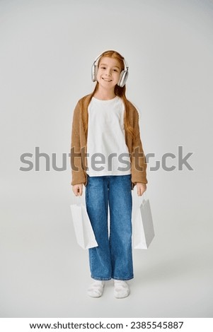 vertical shot of jolly preteen girl posing with present bags and smiling at camera, fashion concept Royalty-Free Stock Photo #2385545887