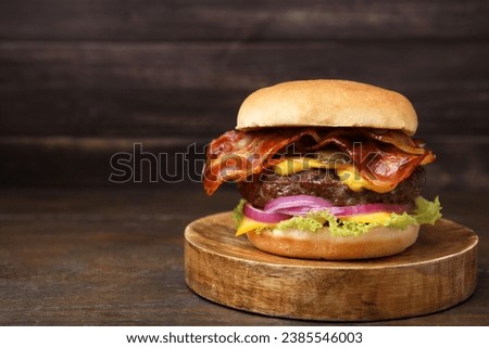 Tasty burger with bacon, vegetables and patty on wooden table, space for text