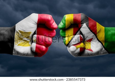 EGYPT vs ZIMBABWE confrontation, religious conflict. Men's fists with painted flags of EGYPT and ZIMBABWE. Dark clouds background