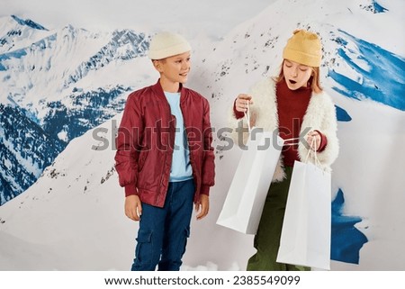 preteen boy looking cheerfully at cute girl looking surprisedly in present bag, fashion concept Royalty-Free Stock Photo #2385549099